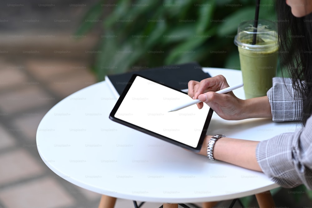 Colpo ritagliato di giovane designer che tiene in mano la penna stilo che disegna sullo schermo della tavoletta digitale mentre è seduto al bar al mattino.
