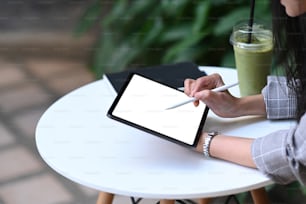 朝、カフェに座りながら、デジタルタブレットの画面にスタイラスペンで描く若いデザイナーのトリミングショット。