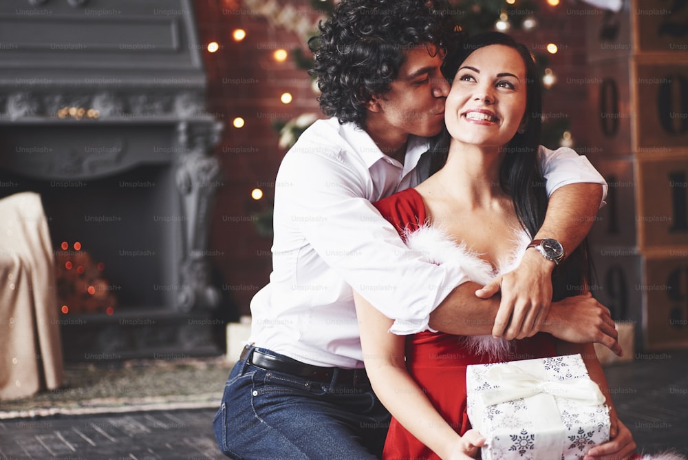 Attractive couple. Woman in red dress holding Christmas gift from boyfriend.