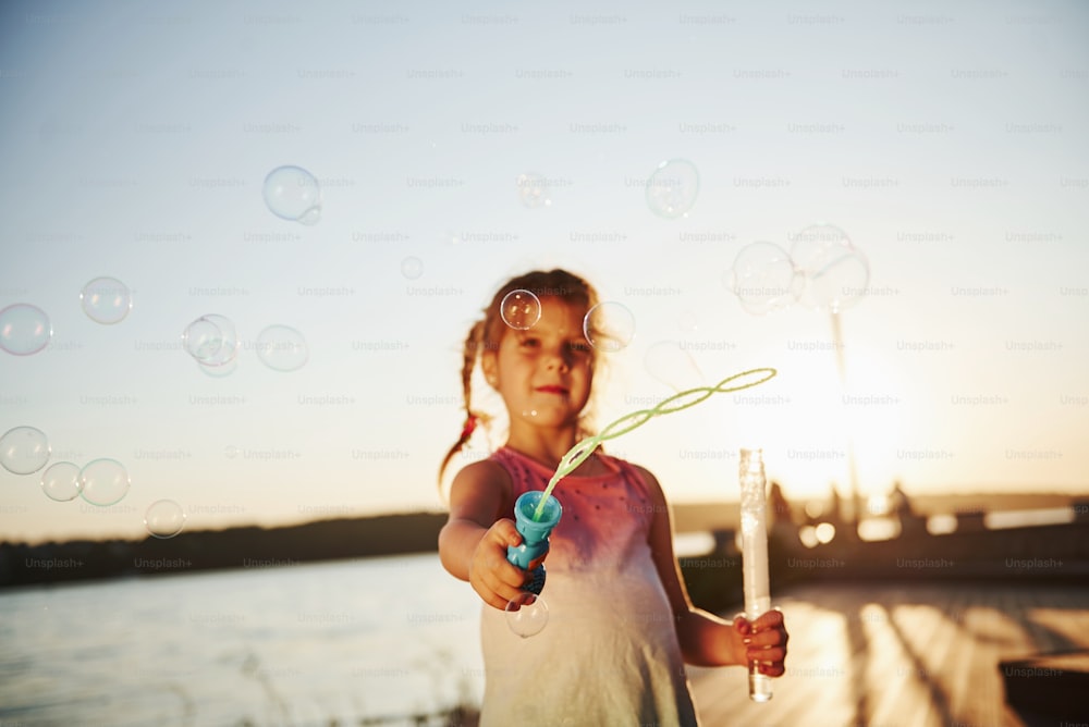 Sera. Bambina felice che gioca con le bolle vicino al lago al parco.