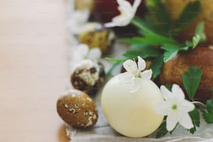 Stylish easter eggs and blooming spring flowers close up on linen napkin on rustic table. Happy Easter! Space for text. Modern natural dyed eggs