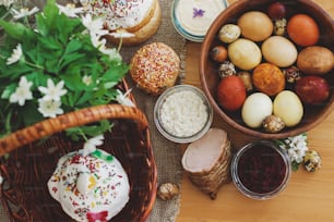 Delicious Easter food, stylish easter eggs, beets, cheese, butter, ham, homemade Easter bread and wicker basket with blooming spring flowers on rustic table, orthodox traditions. Happy Easter!