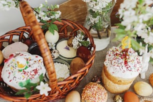 Traditional Easter food for blessing, homemade Easter bread, stylish easter eggs and blooming spring flowers on linen napkin on rustic table. Happy Easter! Festive breakfast