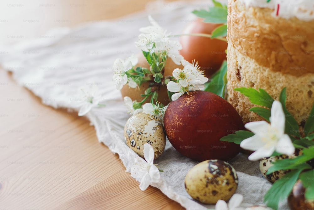 Frohe Ostern! Stilvolle Ostereier, blühende Frühlingsblumen und selbstgebackenes Osterbrot auf rustikaler Tischplatte. Platz für Text. Moderne natürlich gefärbte Eier und traditionelles Osteressen