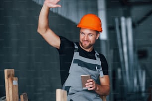 안녕하세요 제스처입니다. 음료 한잔과 함께. 점심 시간. 공장에서 실내��에 있는 쾌활한 산업 노동자. 주황색 안전모를 쓴 젊은 기술자.