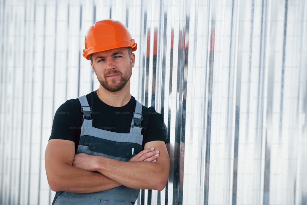 벽에 기대어. 공장에서 실내에 있는 심각한 산업 노동자. 주황색 안전모를 쓴 젊은 기술자.