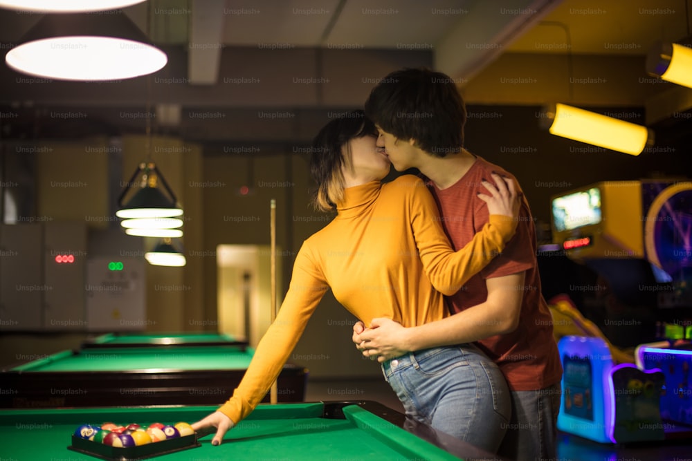 The couple is kissing in the billiard room. Couple in playroom.