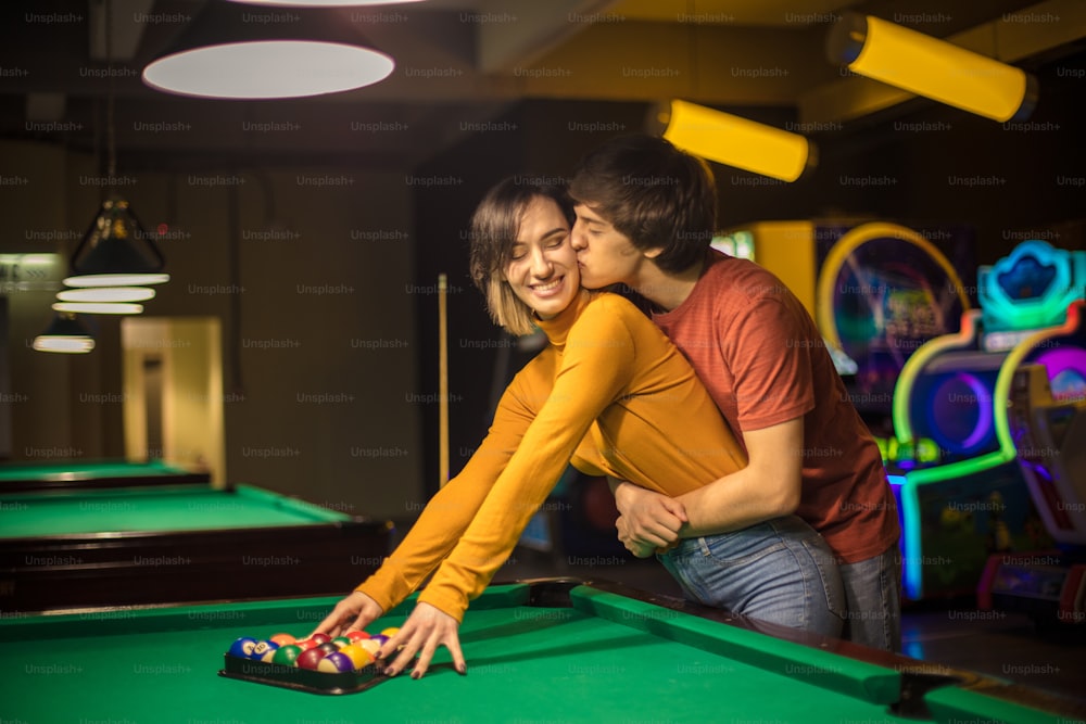 The couple is kissing in the billiard room. Couple in playroom.