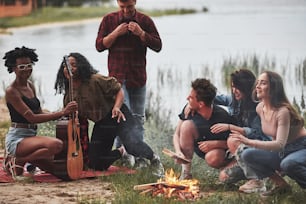 Guardando la chitarra. Un gruppo di persone fa un picnic sulla spiaggia. Gli amici si divertono nel fine settimana.