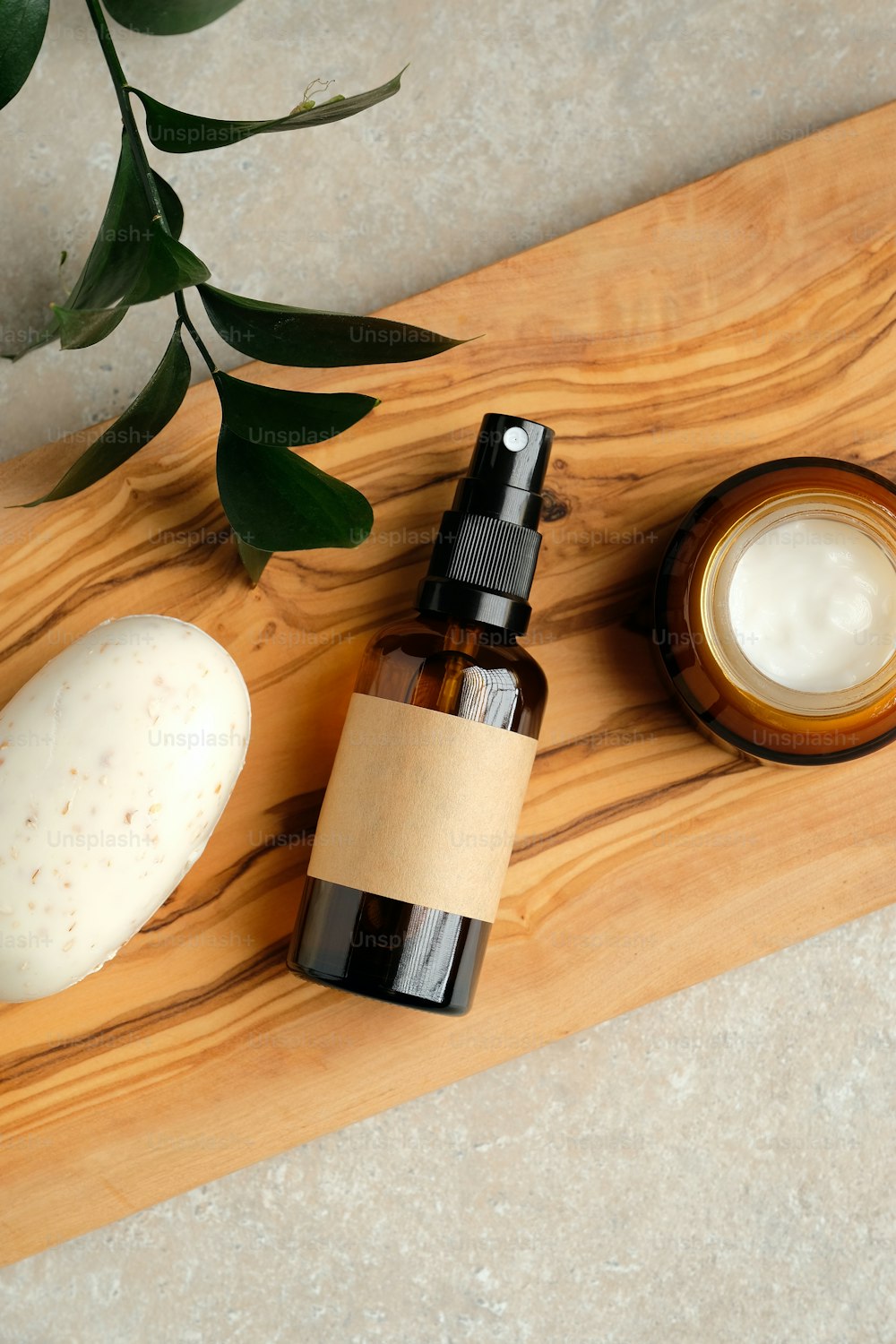 Top view amber glass spray bottle, homemade soap, jar of moisturizer cream on wooden board with green leaf. SPA natural organic beauty product packaging design.