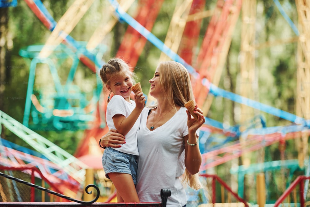 Eating ice cream. Cheerful little girl her mother have a good time in the park together near attractions.