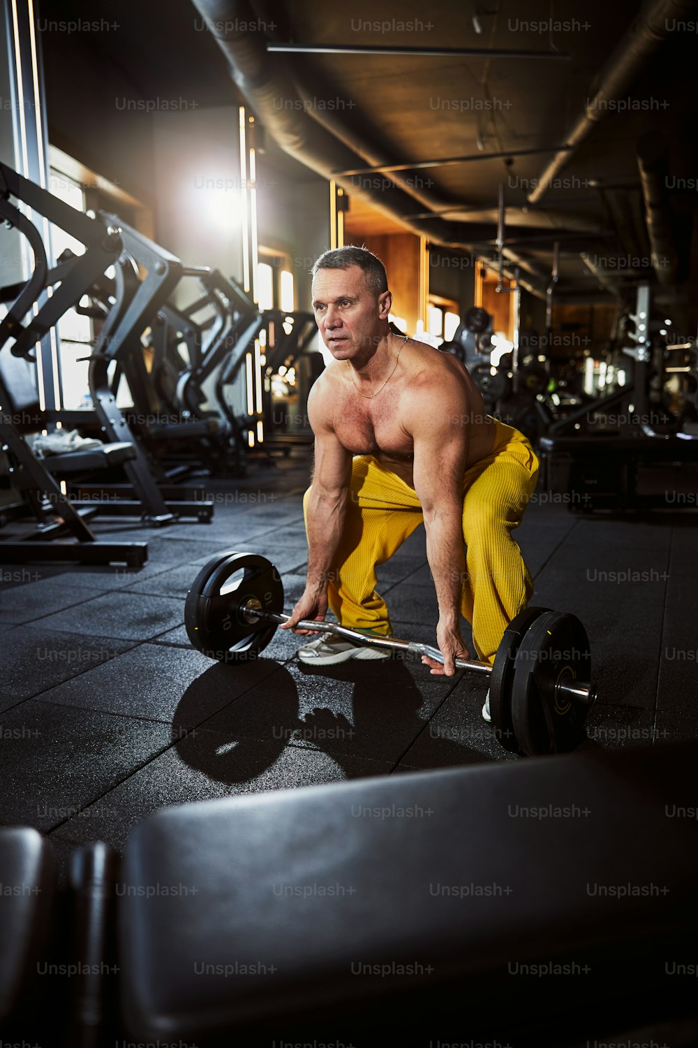 Ernsthafter männlicher Athlet mit nacktem Oberkörper, der sich bückt, um eine Langhantel mit einem schweren Satz Gewichte aufzuheben