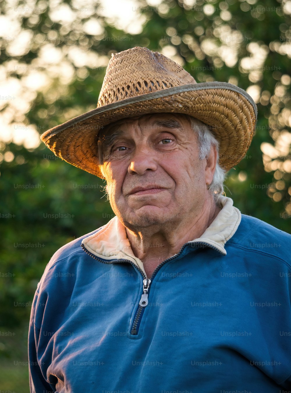 Happy retirement life. An elderly man in a straw hat against the backdrop of a sunny evening garden. Leisure gardening