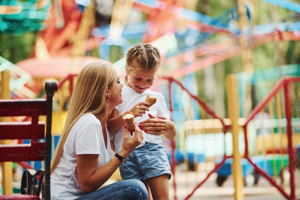 Eating ice cream. Cheerful little girl her mother have a good time in the park together near attractions.