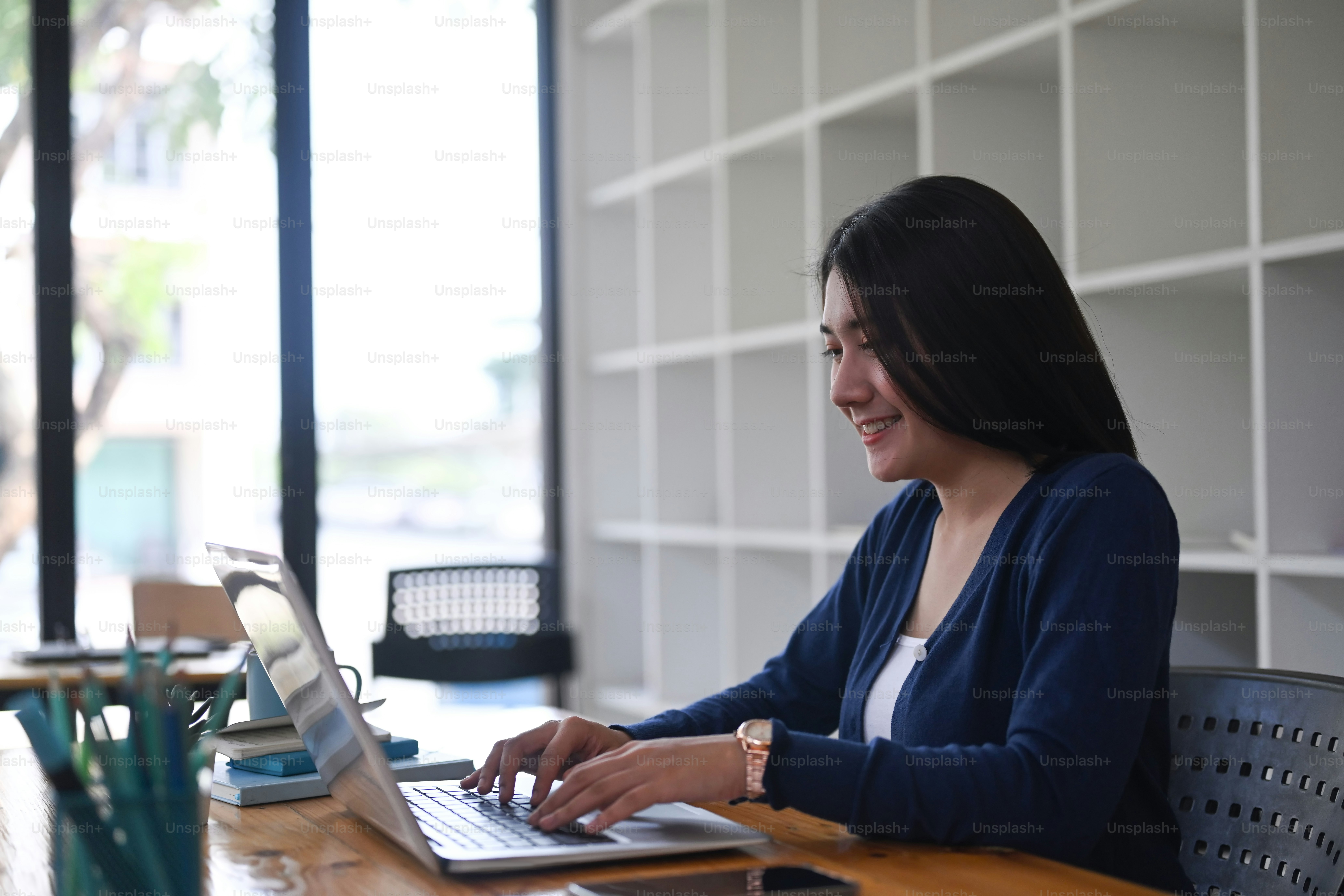 Jeune designer féminine joyeuse souriant et travaillant sur un ordinateur portable au bureau.