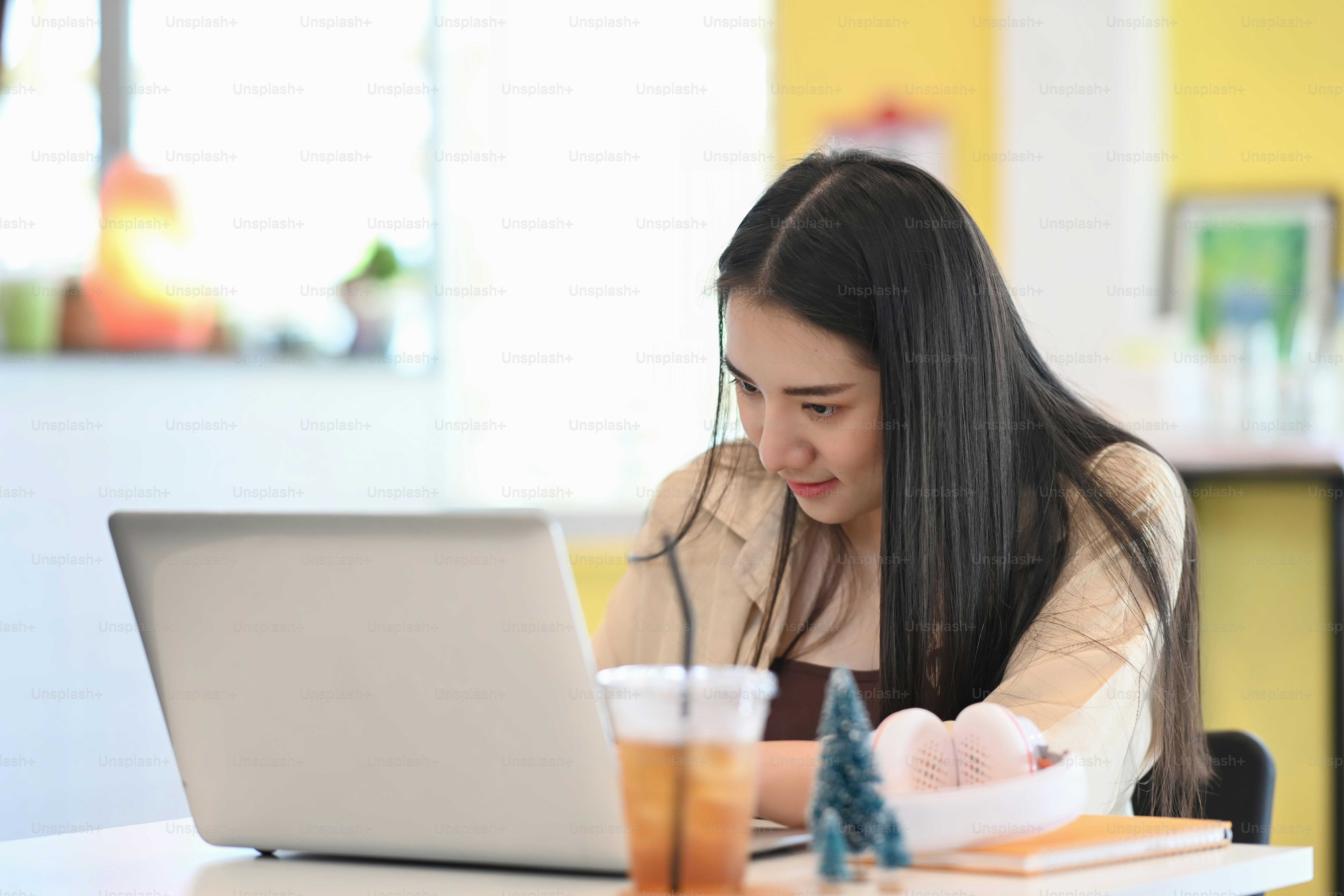 Pekerja lepas wanita muda duduk di tempat kerjanya dan berkonsentrasi bekerja di laptop komputer.