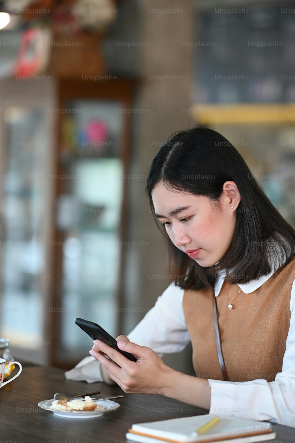 Side view of young asian woman using smart phone while relaxing in coffee shop.