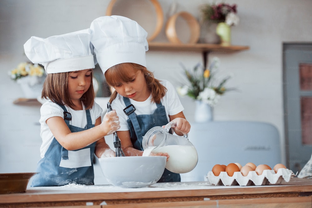 Family kids in white chef uniform preparing food on the kitchen.