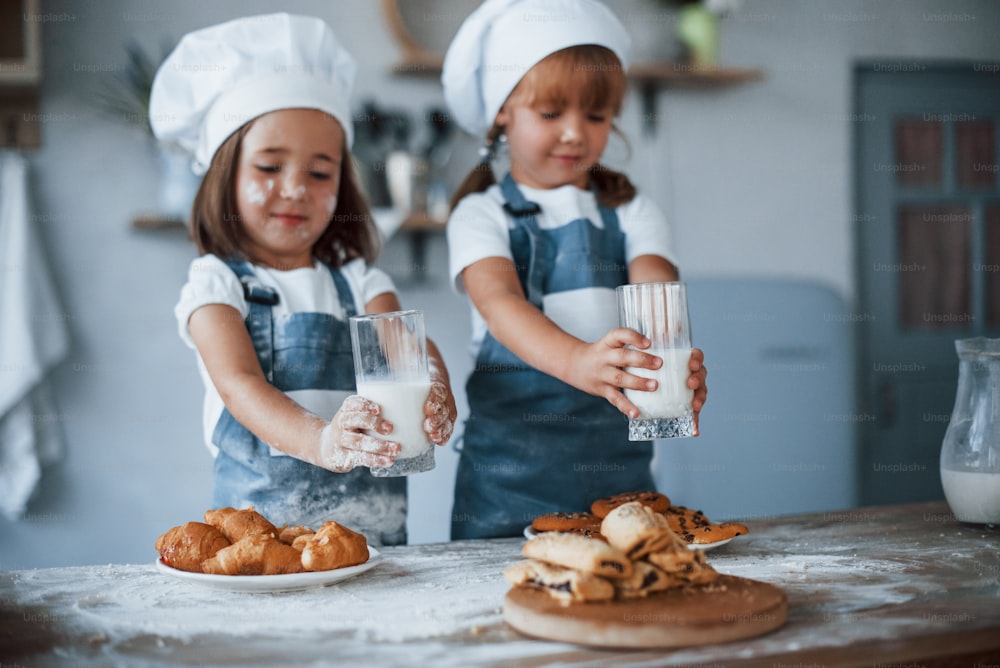 Con bicchieri con latte. Bambini della famiglia in uniforme bianca da chef che preparano il cibo in cucina.
