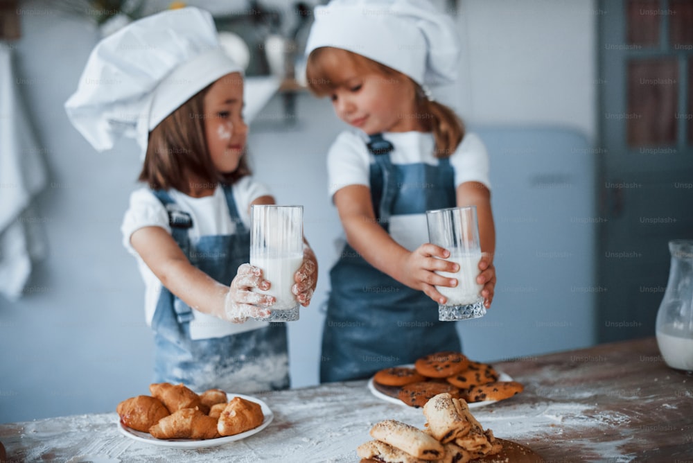 Con vasos con leche. Niños de la familia con uniforme de chef blanco preparando comida en la cocina.