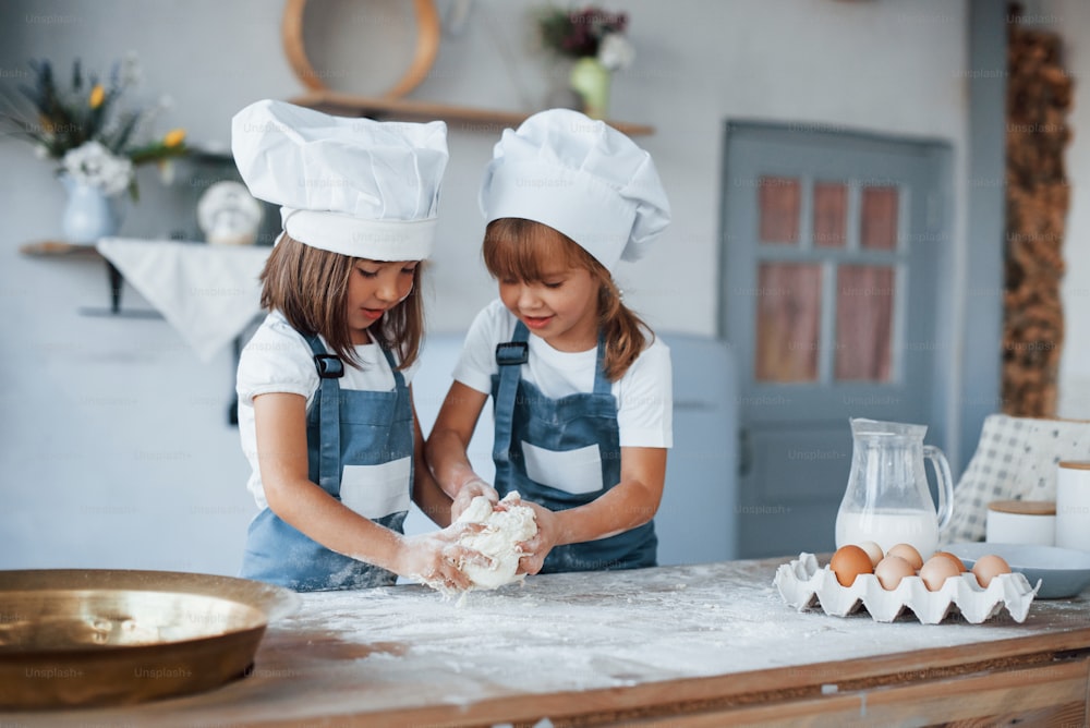 Family kids in white chef uniform preparing food on the kitchen.