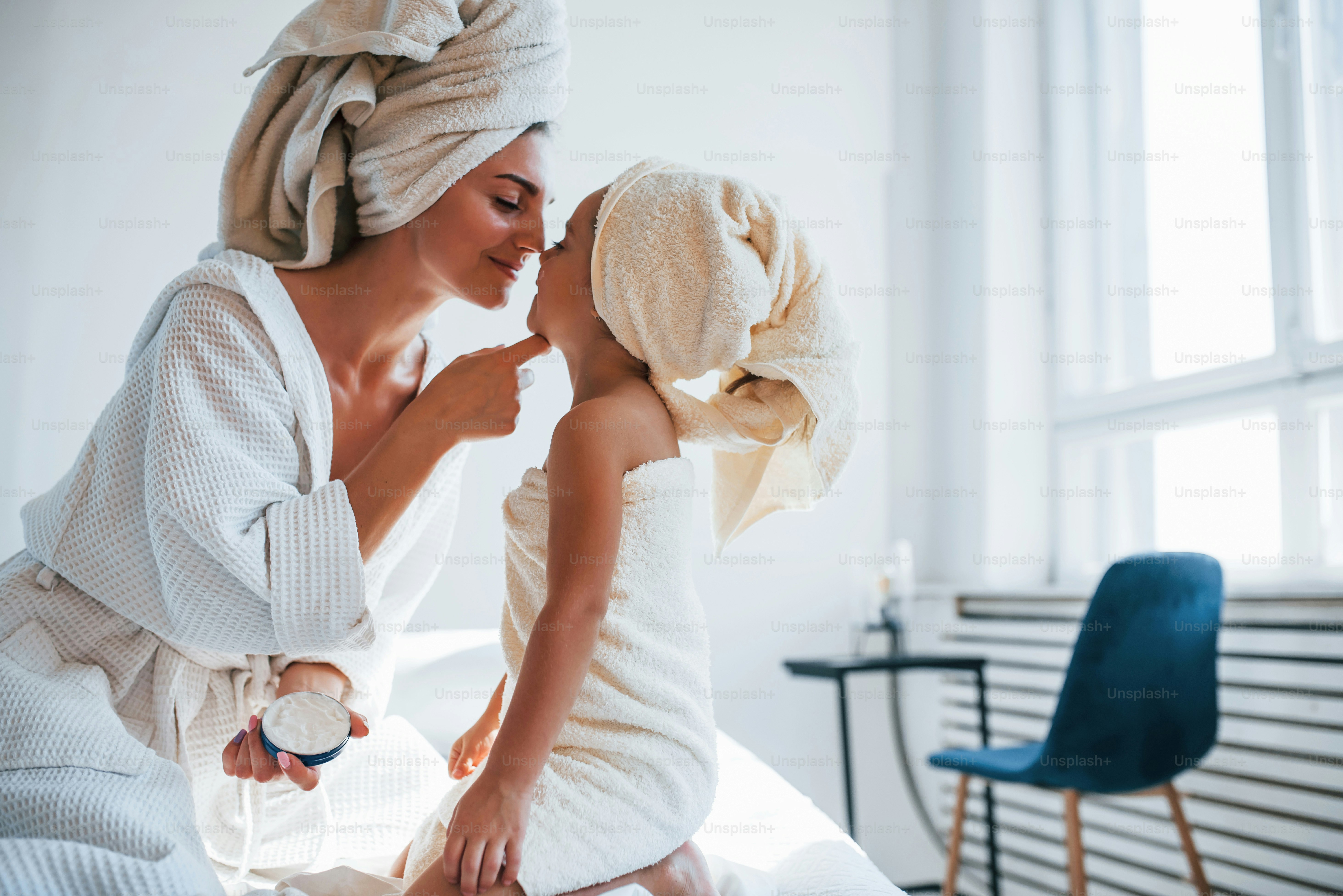 Usare la crema per schiarire la pelle. La giovane madre con la figlia ha una giornata di bellezza al chiuso in una stanza bianca.