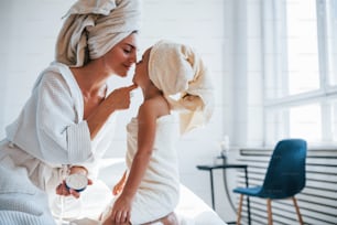 Using cream to clear skin. Young mother with her daugher have beauty day indoors in white room.