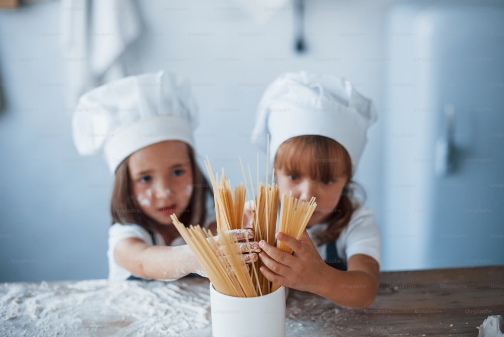 S’amuser avec des spaghettis. Des enfants de la famille en uniforme de chef blanc préparent de la nourriture dans la cuisine.