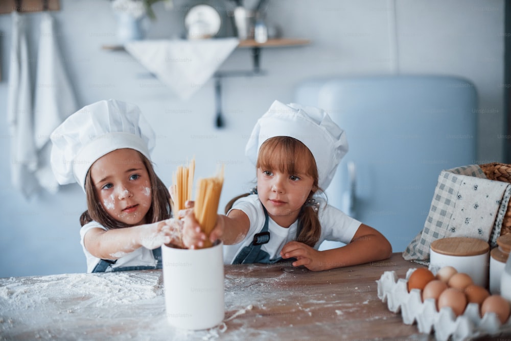 Divertirsi con gli spaghetti. Bambini della famiglia in uniforme bianca da chef che preparano il cibo in cucina.