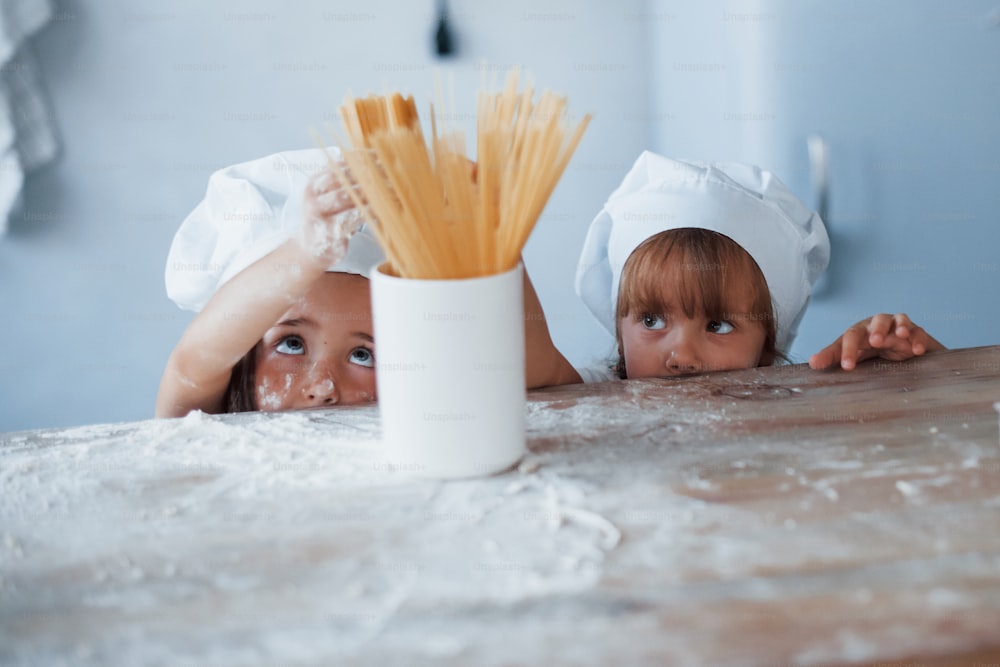 스파게티와 함께 즐거운 시간을 보내십시오. 부엌에서 음식을 준비하는 흰색 요리사 유니폼을 입은 가족 아이들.