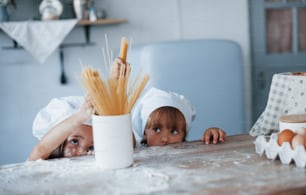 Divertirsi con gli spaghetti. Bambini della famiglia in uniforme bianca da chef che preparano il cibo in cucina.