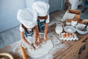 Vista superior. Crianças da família em uniforme de chef branco preparando comida na cozinha.