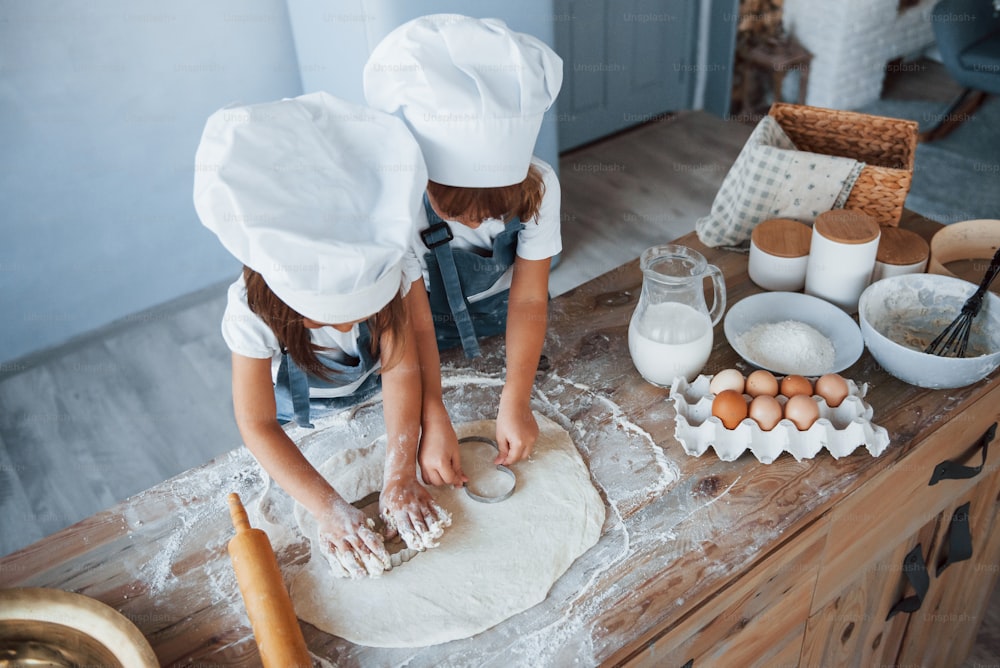Vista superior. Niños de la familia con uniforme de chef blanco preparando comida en la cocina.