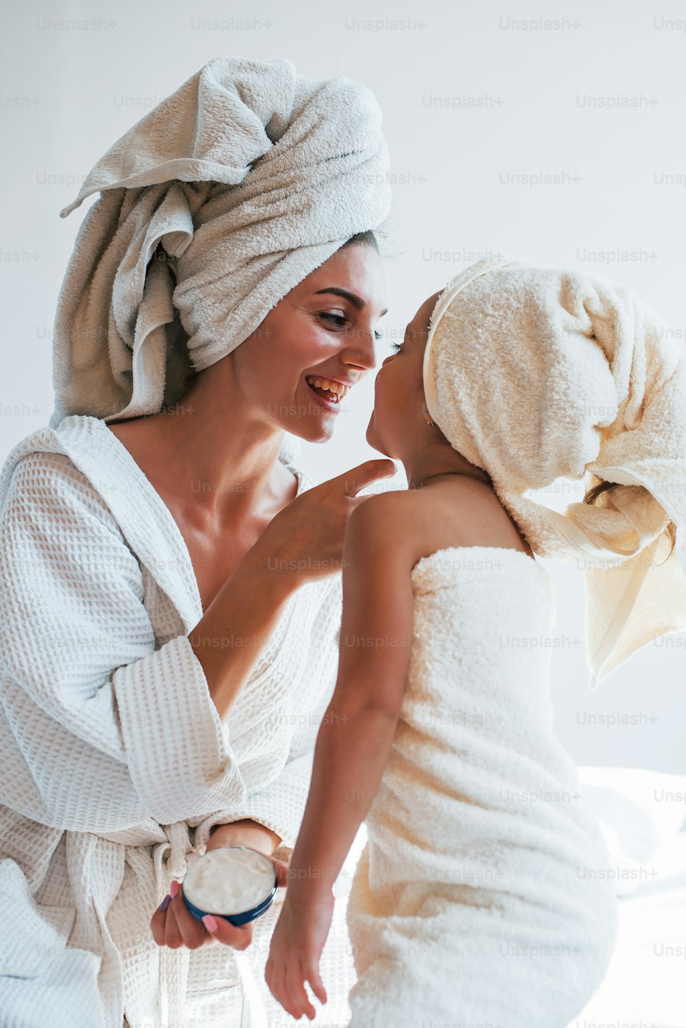크림을 사용하여 피부를 맑게합니다. 그녀의 daugher와 함께 젊은 어머니는 하얀 방에서 실내에서 아름다움의 날을 보낸다.