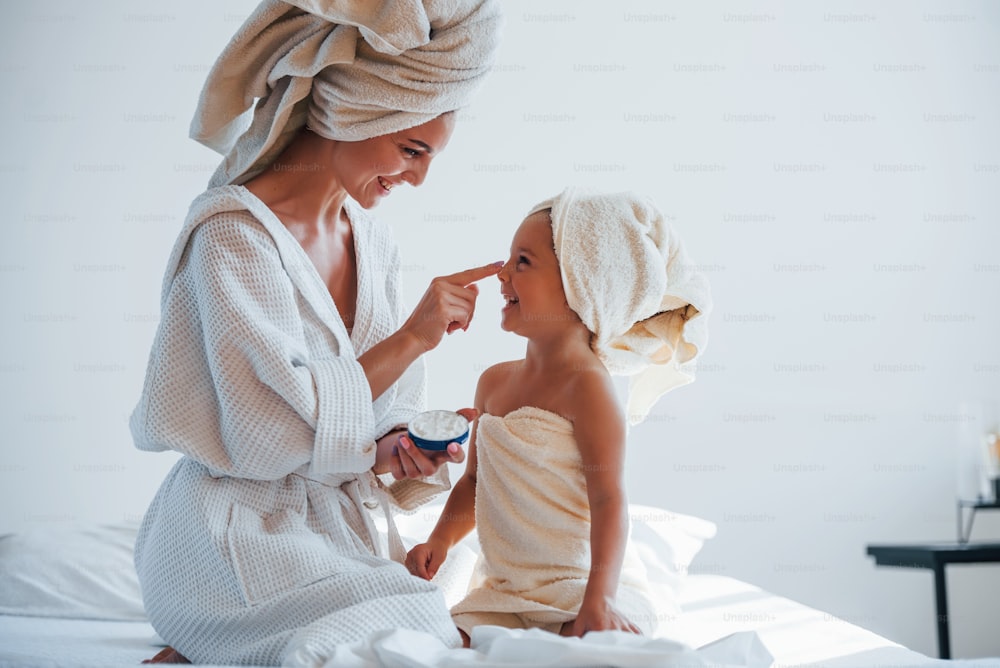 Using cream to clear skin. Young mother with her daugher have beauty day indoors in white room.