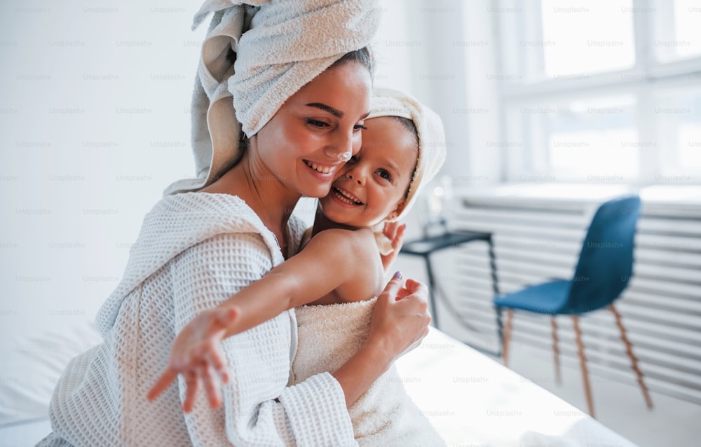 Young mother with her daugher have beauty day indoors in white room.