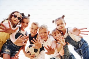 Hello, gesture. With soccer ball. Portrait of kids that standing together and posing for the camera.