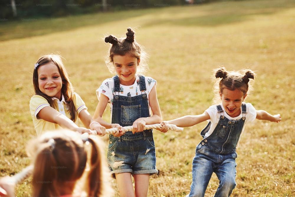 Kids playing tug of war game in the beautiful meadow at sunny day.