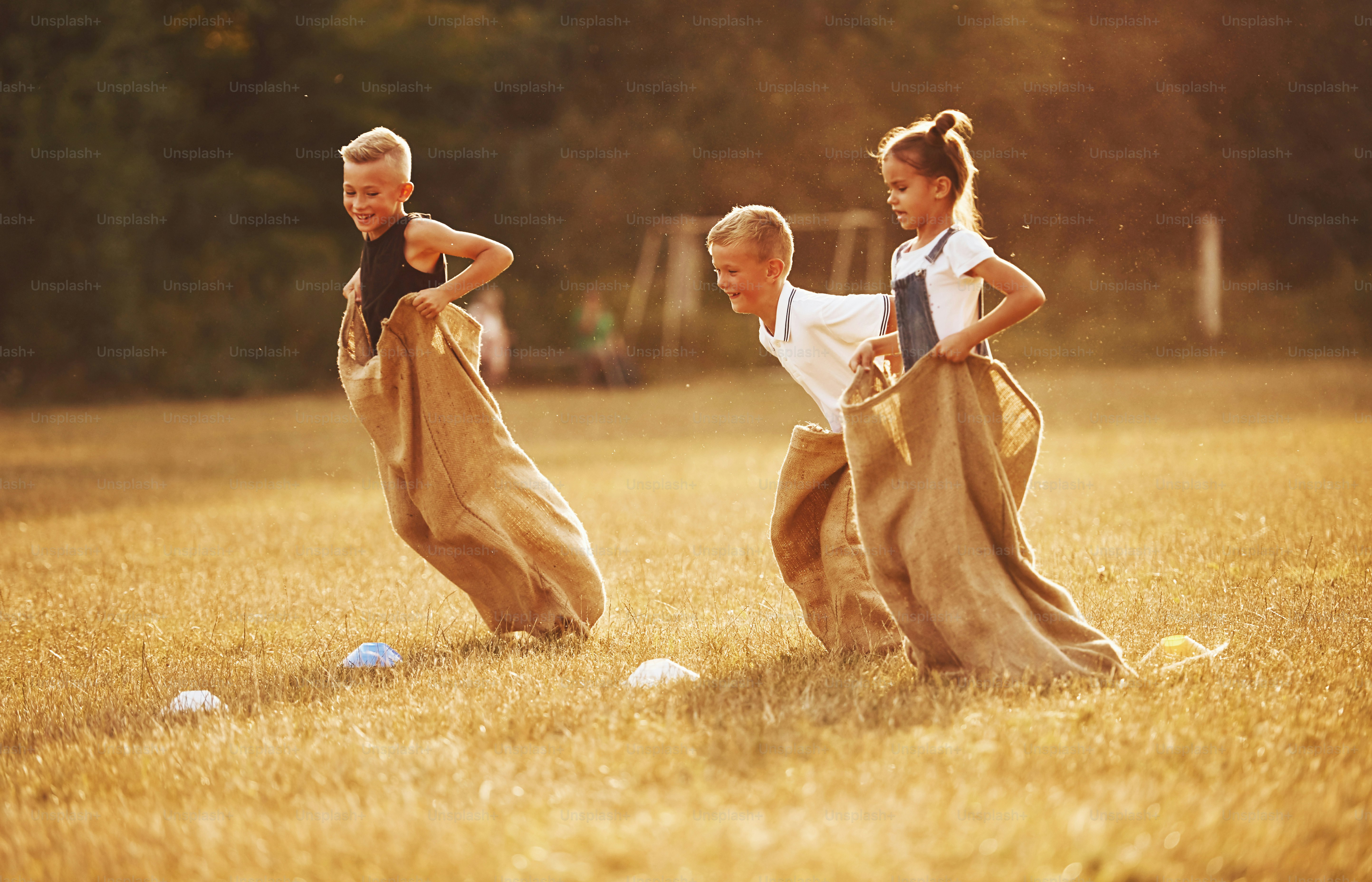 Jumping sack race outdoors in the field. Kids have fun at sunny daytime.