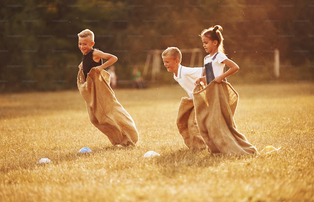 Carrera de sacos de salto al aire libre en el campo. Los niños se divierten durante el día soleado.