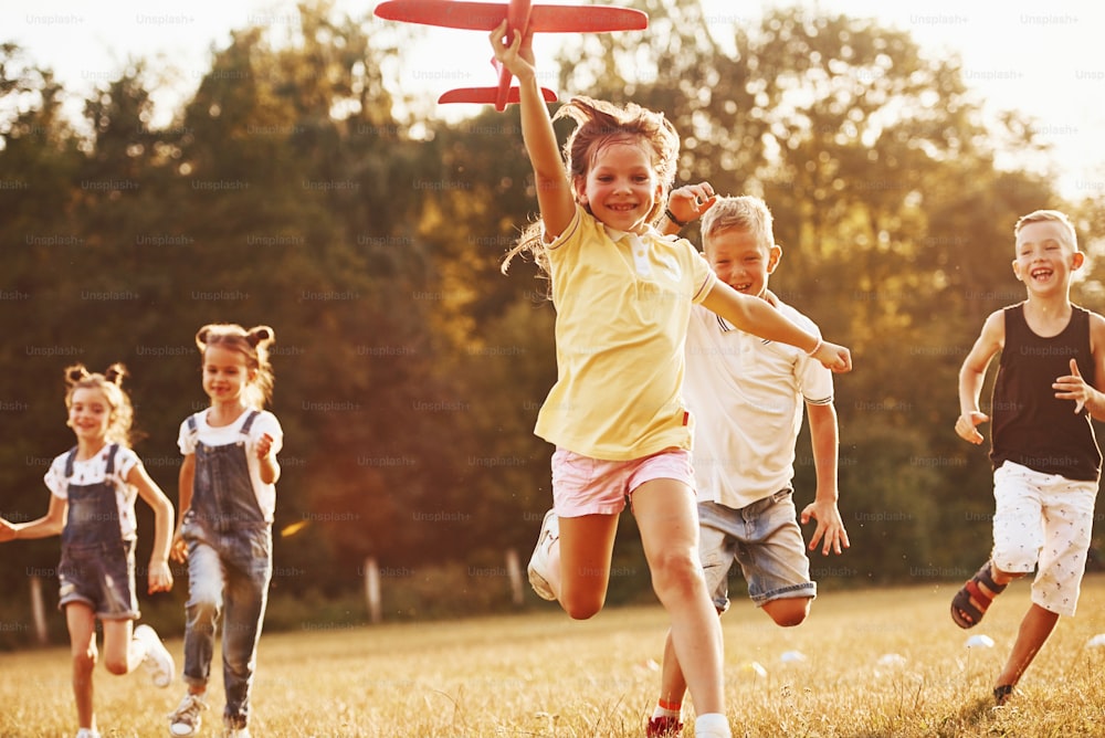 Grupo de niños divirtiéndose al aire libre con un avión de juguete rojo en las manos.