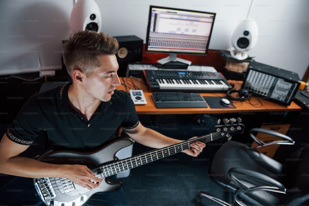 Young musician records bass guitar indoors in the studio.