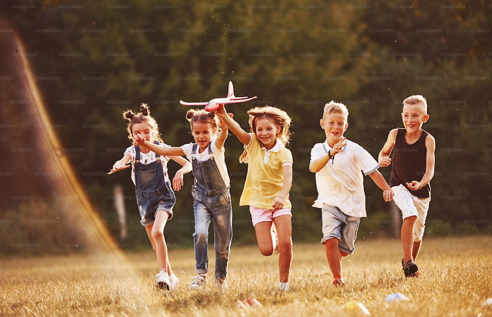 Group of kids having fun outdoors with red toy airplane in hands.