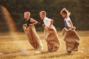 Corsa con i sacchi saltando all'aperto nel campo. I bambini si divertono nelle giornate di sole.