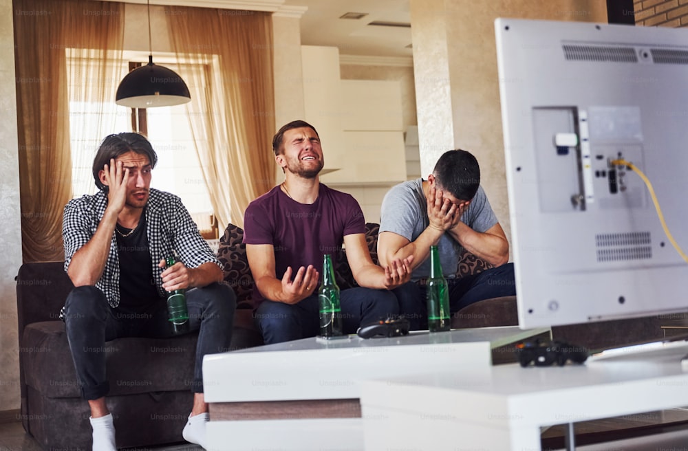 É uma derrota. Tristes três amigos assistindo futebol na TV em casa juntos.