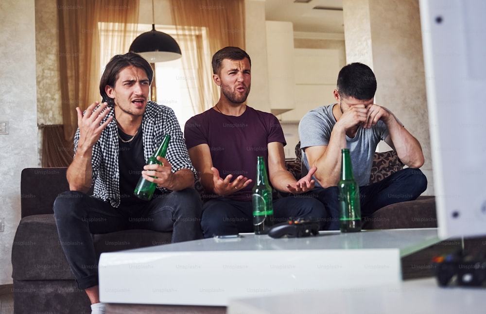 É uma derrota. Tristes três amigos assistindo futebol na TV em casa juntos.