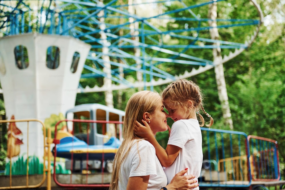 Loving each other. Cheerful little girl her mother have a good time in the park together near attractions.