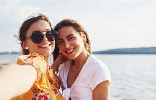 晴れた日に湖を背景に楽しい週末を過ごす屋外の笑顔の2人の女の子の自撮り。