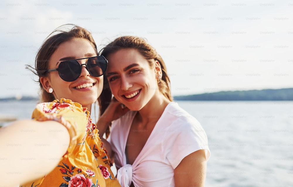 Selfie di due ragazze sorridenti all'aperto che trascorrono un buon fine settimana insieme in una giornata di sole contro il lago.