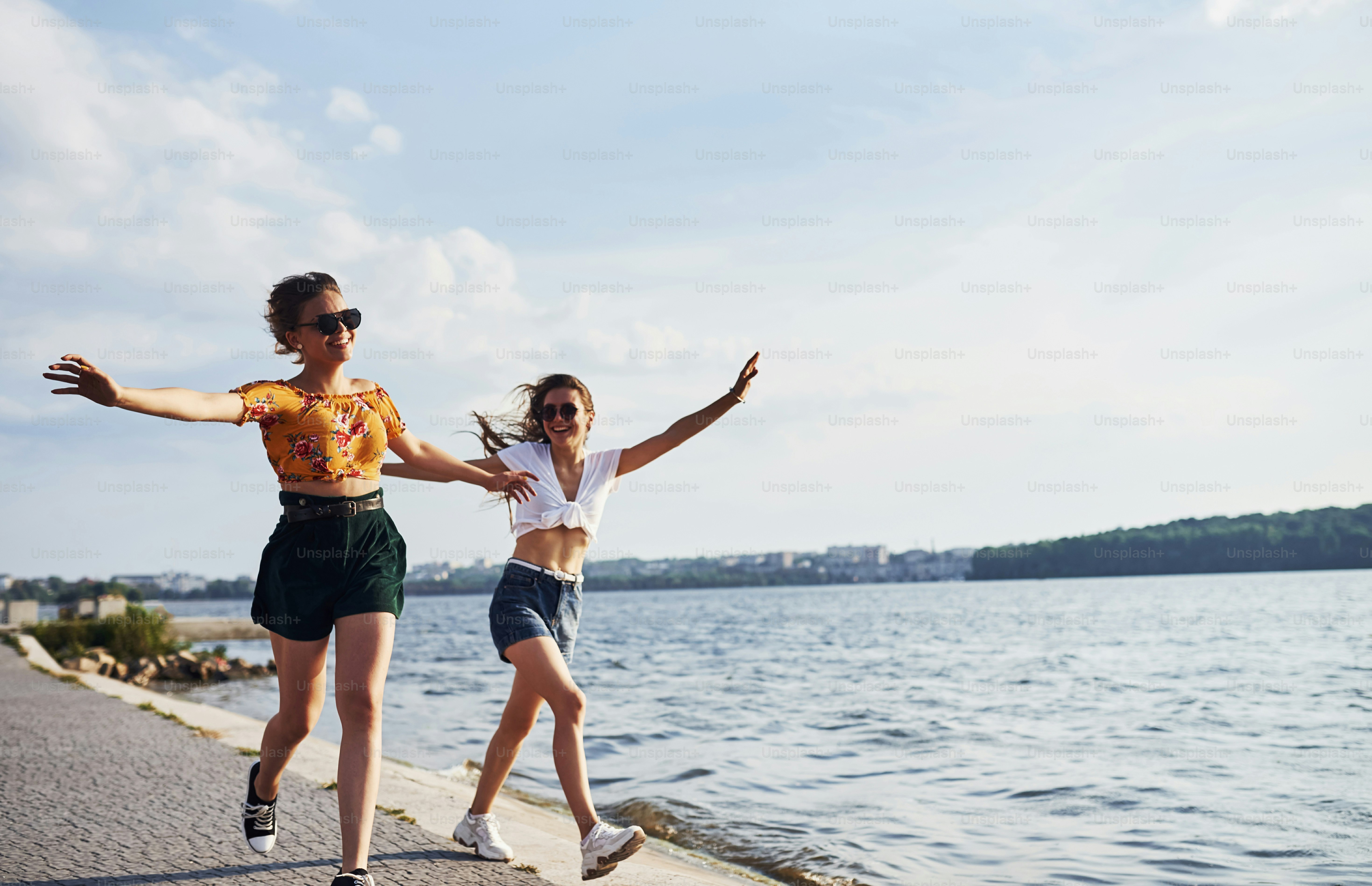 Two female friends runs and have fun at beach near the lake at sunny daytime.